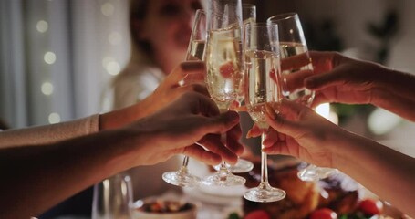 Hands with glasses of champagne clink glasses over the festive table. Celebration of New Year and Christmas