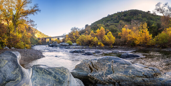 Panoramic view of autumn foliage and boulders by the Golo river as it passes under the Pont d'Albano railway bridge at the Torrent de Cipetto near Barchetta in Corsica