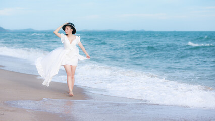 Fototapeta na wymiar Young asian woman wearing white dress and black hat walking relax on the beach, enjoying the sea and Happy summer vacation
