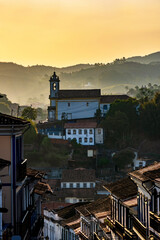 Old church seen in the city of Ouro Preto during sunset with its houses in colonial architecture, roofs and the mountains in the background