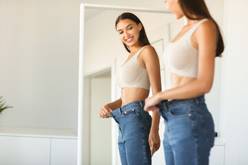 Excited young fit woman losing weight and wearing old big jeans, woman feeling satisfied with...