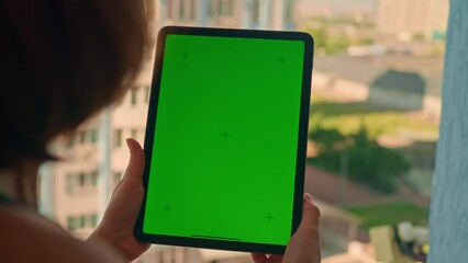 unrecognizable woman holding digital tablet with green screen standing in front of opened window