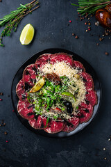Beef carpaccio: beef tenderloin, romaine lettuce, sun-dried tomatoes, parmesan cheese, top view.
