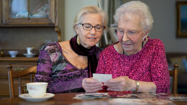 Senior elderly smiling happy woman looking at old photos and remembering memories with daughter at the dining room table.