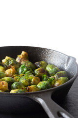Sprouts fried, in a cast iron frying pan wiyth olive oil, on a slate board. Isolated on a white background