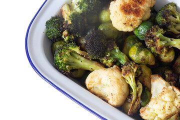 Brussels sprouts, cauliflower and broccoli, oven roasted in olive oil,  in an enamel dish bowl. Isolated on a white background