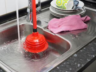 Kitchen sink full of dirty water, red plunger