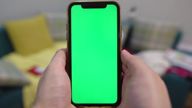 Use green screen for copy space closeup. in front of a desktop with a laptop. Chroma key mock-up on smartphone in hand.  young man holds mobile phone iPhone and swipes photos or pictures