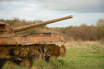 a view along the side and gun barrel of an abandoned rusting British FV4201 Chieftain main battle tank wreck in afternoon sunlight