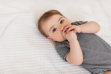 Child care concept. Cute little baby lying on bed, girl wearing bodysuit and wetting the pacifier, copy space