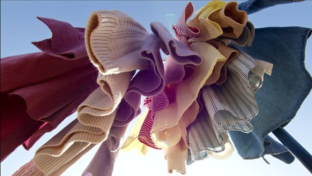 Low angle view of colourful clothes hanging on rail outdoors against blue sky.