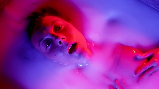 Slow-motion shot of a sensual woman taking a bath with milk in neon light psychological portrait