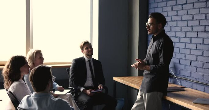 Confident skilled businessman trainer lead seminar for corporate staff meet in office, makes speech, share knowledge and professional experience, talking, to diverse company employees. Briefing event