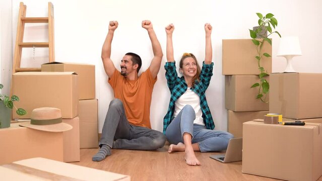 Couple with moving boxes happy celebrating in their new home household move. Attractive young friends in love smiling together. High quality 4k footage