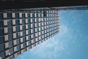 Hochhaus mit vielen Fenster von unten aus und einen blauen Himmel mit Wolken