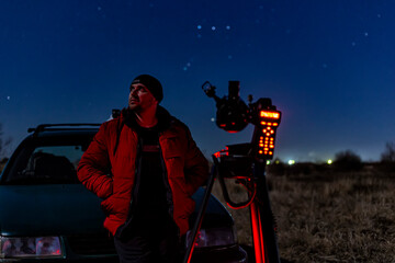 A man against the background of a dark sky, the constellation of Orion in red light from a...