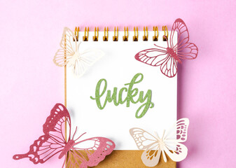 The Lucky text on diary and paper butterfly on pink colour background.