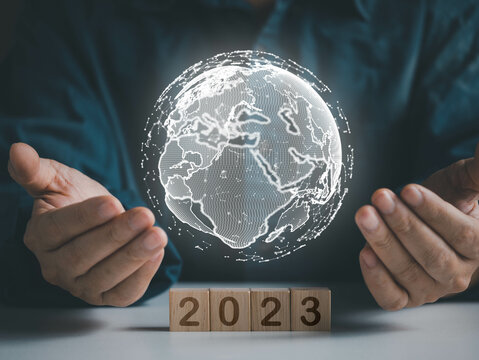 Hand holding virtual earth over wood cube within wording 2023, happy new years 2023 concept.