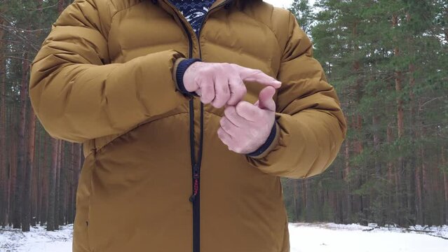 A man in a mustard down jacket bends his fingers on his hands, listing or counting something while standing in a forest.