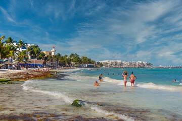 PLAYA DEL CARMEN, MEXICO - APR 2022: Pretty young girl in sexy brazilian bikini is walking and carrying her bag along the beach with waves