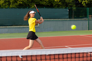 Professional equipped female tennis player beating hard the tennis ball with racquet.