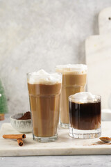 Three tall glasses with warm coffee drink with cinnamon, whipped milk foam and caramel on a marble board and christmas ornaments and decoration