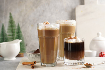 Three tall glasses with warm coffee drink with cinnamon, whipped milk foam and caramel on a marble board and christmas ornaments and decoration