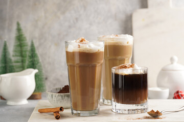 Three tall glasses with warm coffee drink with cinnamon, whipped milk foam and caramel on a marble...