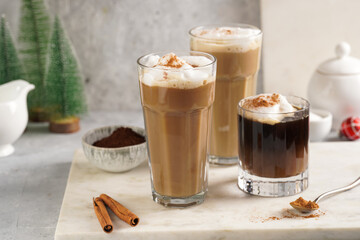 Three tall glasses with warm coffee drink with cinnamon, whipped milk foam and caramel on a marble board and christmas ornaments and decoration