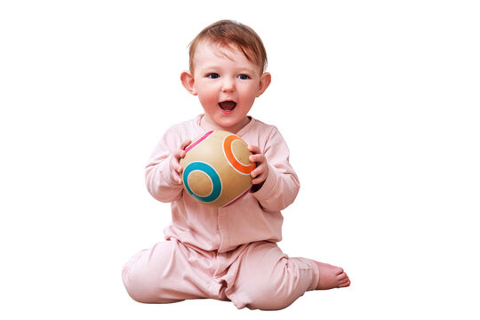 Happy toddler baby boy throws a ball with his hands while sitting on the floor in the home room, isolated on a white background. A child aged one year