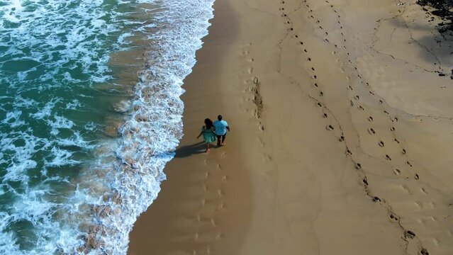 aerial drone footage of a black couple walking across the nice sandy beaches of Dominican Republic Punta Cana. the roman pair are on holiday enjoying a  relaxing tropical lifestyle.