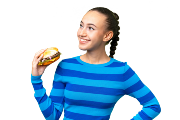 Young Arab woman holding a burger over isolated background posing with arms at hip and smiling