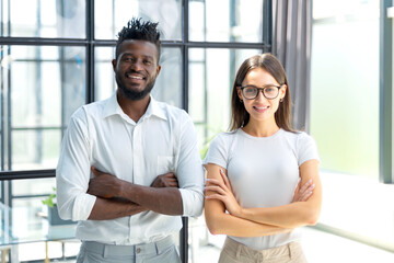 African woman and caucasian man looking at camera standing in office. Multicultural company...