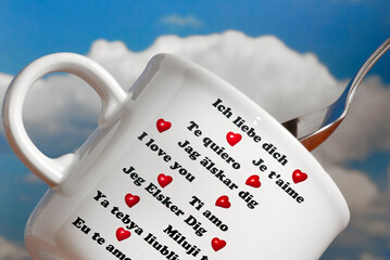 white coffee or tea cup with text I love you in various languages and red heart over blue sky like...