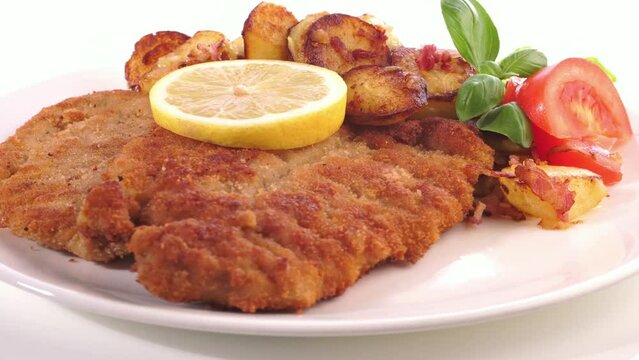 Wiener Schnitzel paniert auf einem Teller mit Bratkartoffel auf wei&szlig;em Hintergrund - Drehteller