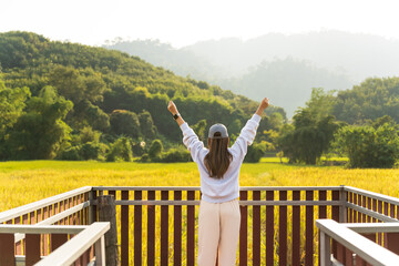 Woman traveler stand at terrace in the natural resort or hotel style to sightseeing paddy field on mountain background.Bak view of young girl enjoying beauty of nature looking at mountain.