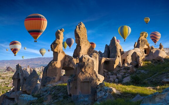Welcome to Cappadocia concept image. Hand carved rooms in limestone rocks in Cappadocia, Turkey. Hot air balloons fly in blue sky.