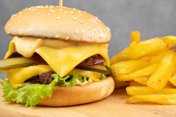 Hamburger with tomatoes, pickles and cheese. Nearby is a portion of french fries