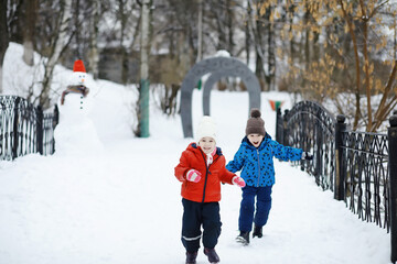Fototapeta na wymiar Children in the park in winter. Kids play with snow on the playground. They sculpt snowmen and slide down the hills.
