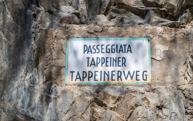 Bilingual signpost of Tappeinerweg in german and italian, Passeggiata Tappeiner, on a stonewall....