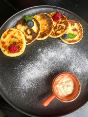 Curd Cheese or cottage Cheese fritters, syrniki served with sour cream, raspberries and blueberry. Table top view. Ukrainian, Russian cuisine breakfast meal.