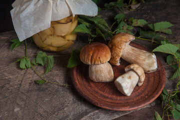 Clay plate with porcini mushroom commonly known as Boletus Edulis and glass jar with canned mushrooms on vintage wooden background..