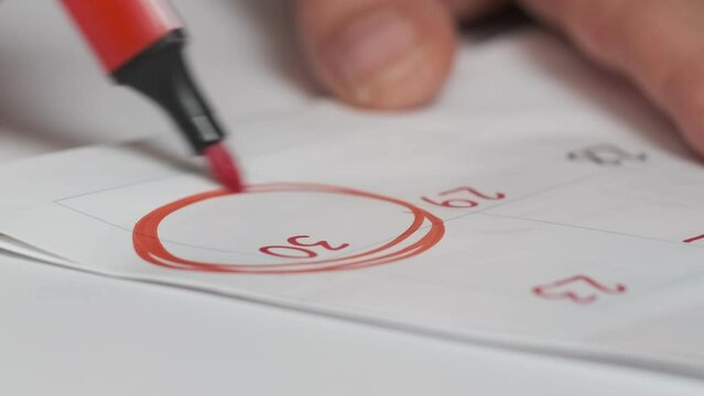 woman's hand circles the last day of the month. concept of deadline or end of month. A person marks an important date on a wall calendar