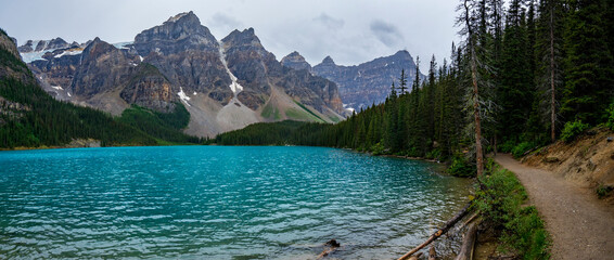 Panoramic view of Moraine Lake in a cloudy summer afternoon from the footpath by the lake.