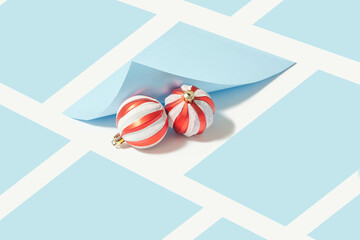 Creative composition with two red Christmas baubles under a pastel blue folded sheet of paper. Geometric background. Minimal xmas holidays concept.