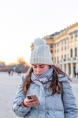 Woman checking news and text on her cellphone outdoor during cold winter season.