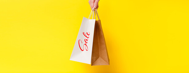 Sale, special offer banner. Female hand holding two shopping bags isolated on yellow background. Black friday sale, discount, shopping and ecology concept.