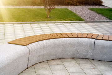 Curiously curved concrete bench with wooden slats for sitting in city park at autumn - obrazy, fototapety, plakaty