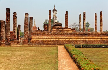 Fototapeta na wymiar View of a Buddha statue seated among decadent columns of a ruined shrine in Wat Mahathat, an ancient Buddhist Temple and a beautiful UNESCO heritage site in Sukhothai Historical Park in Thailand, Asia