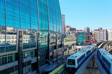 View of a train traveling on elevated rails of Taipei Metro System by a modern building of glass curtain walls on a beautiful sunny day ~ View of MRT railways in Taipei, the capital city of Taiwan